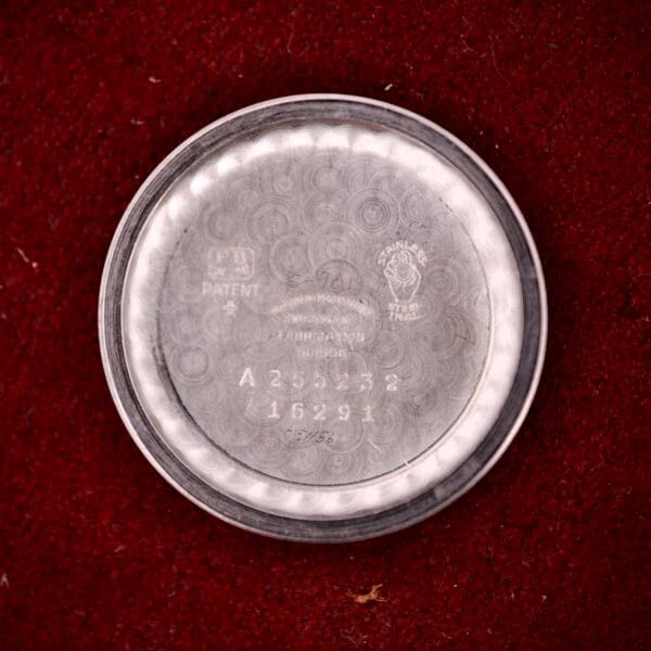 A round stainless steel case back from a Movado Automatic Date Ref. 16291 Bumper Cal. 224A, with Cal. 224A engravings, rests on a red textured surface.