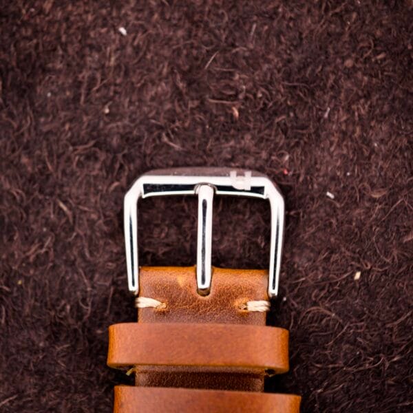 Close-up of a brown leather belt with a silver buckle on a dark background, inspired by the classic craftsmanship of the Omega Ref. 2496 Arabic Numerals Stainless Steel Case Cal. 30T2 SC timepiece.