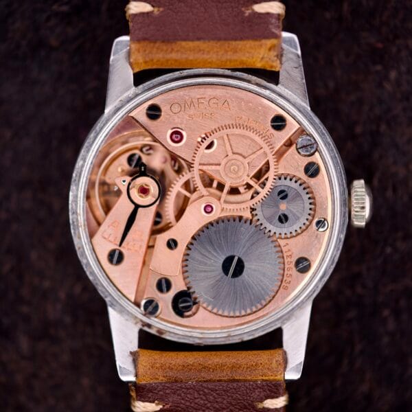 Close-up of the Omega Ref. 2496, featuring Arabic numerals on the dial, an exposed Cal. 30T2 SC movement, stainless steel case, visible mechanical gears, and a brown leather strap.