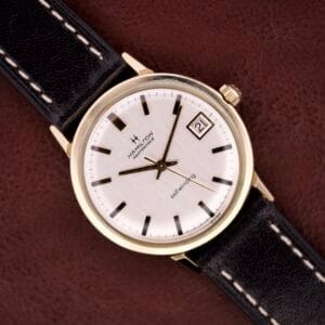 Hamilton Masterpiece Self-Winding Date wristwatch with 10K gold-filled case, white dial, black markers, date window, Cal. 822 movement, and black leather strap.