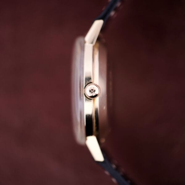 Close-up side view of a Hamilton Masterpiece Self-Winding Date in 10K GF Case Cal. 822 with a black leather strap, set against a brown background.