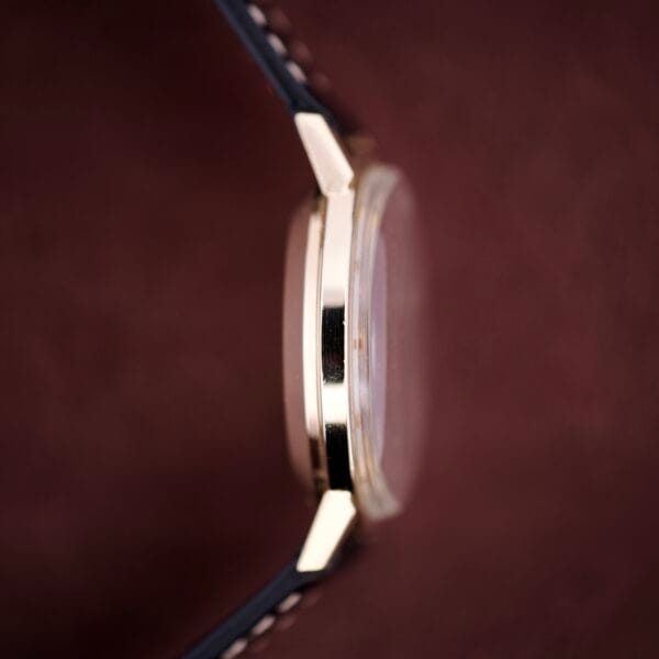 Close-up side view of a Hamilton Masterpiece Self-Winding Date in 10K GF Case Cal. 822 with a black leather strap, set against a burgundy background.