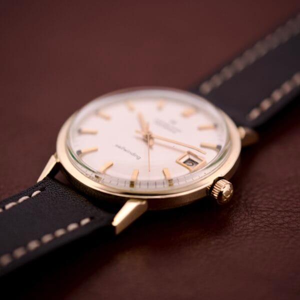 Hamilton Masterpiece Self-Winding Date in 10K GF Case Cal. 822, featuring a white dial and black leather strap, displayed on a brown surface.