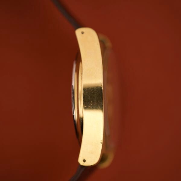 Side view of the Tissot Seastar PR 516 GL Maroon Dial Ref. 46572 Day/Date Cal. 794 with a gold case, brown strap, and maroon dial, set against a reddish-brown background.