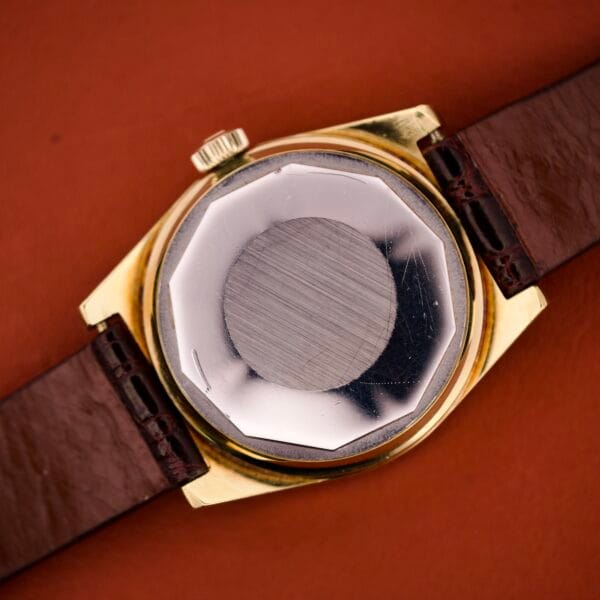 The Tissot Seastar PR 516 GL Maroon Dial Ref. 46572, featuring a day/date display, gold case, and brown leather strap, is shown from the back on a brown surface.