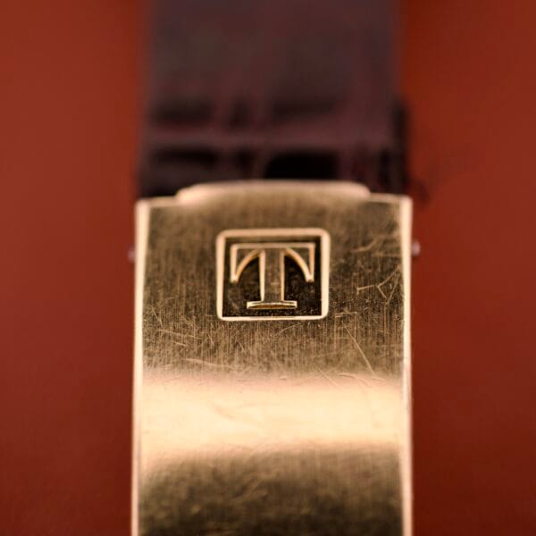 Close-up of the gold clasp with engraved T logo on a textured band, highlighting the maroon dial and day-date display of the Tissot Seastar PR 516 GL Maroon Dial Ref. 46572 Cal. 794 for a refined, classic look.