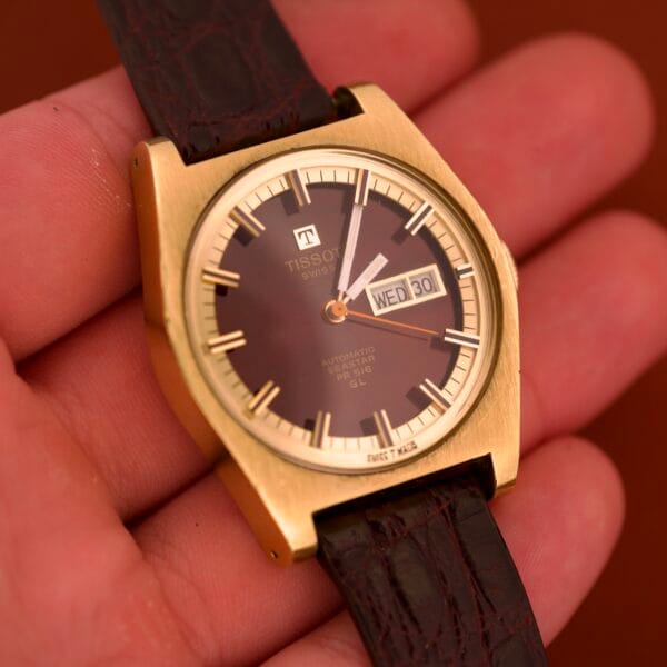 A hand holds a Tissot Seastar PR 516 GL Maroon Dial Ref. 46572, featuring day/date Cal. 794 and paired with a dark leather strap.