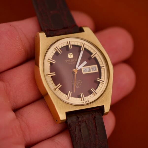 A hand holds a Tissot Seastar PR 516 GL Maroon Dial Ref. 46572 wristwatch with day/date display and black leather strap.