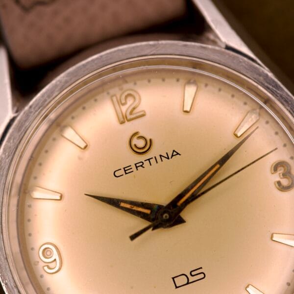 Close-up of a Certina DS Ref. 346.825 1st Gen Cal. 25-36 wristwatch in a stainless steel case, displaying 2:49 on its beige dial with gold hands.