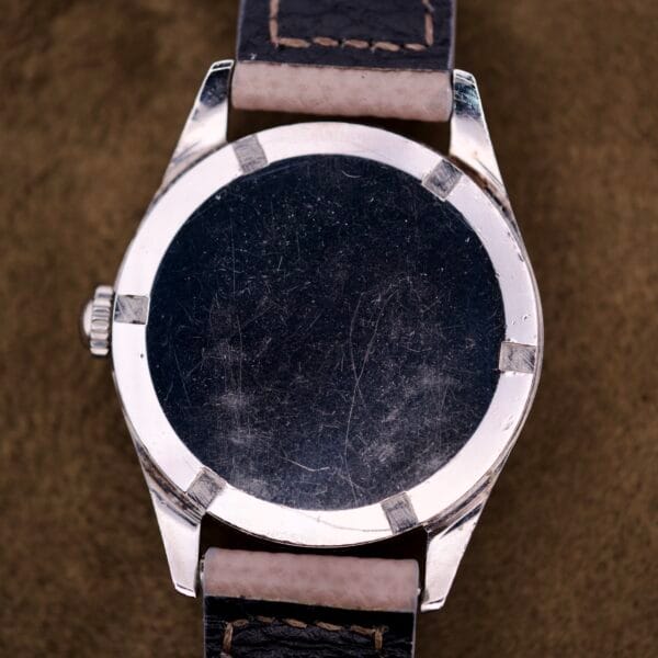 A close-up of the back of a scratched, round Certina DS Ref. 346.825 1st Gen Cal. 25-36 wristwatch with a black leather strap and stainless steel case.