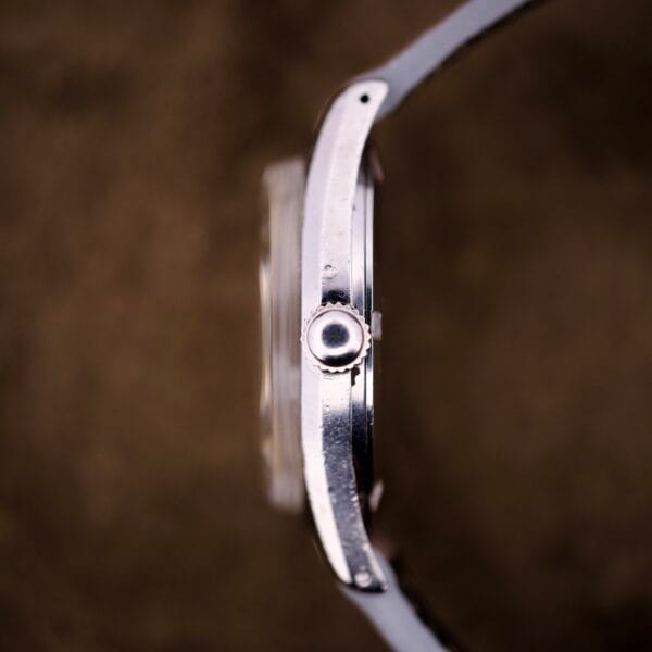Side view of a Certina DS Ref. 346.825 1st Gen wristwatch featuring a stainless steel case and Cal. 25-36 movement, set against a blurred brown background.