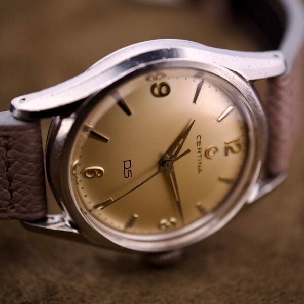 Close-up of a Certina DS Ref. 346.825 1st Gen Cal. 25-36 wristwatch with gold dial, brown leather strap, and classic stainless steel case.