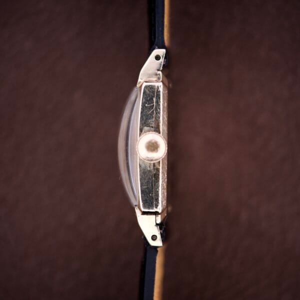 Side view of a Hamilton Tank 14k Gold Filled Case Manual Wind Cal. 982 U.S.A. wristwatch with black strap and brown textured background.