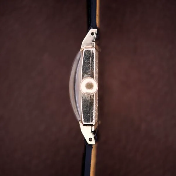 Side view of a Hamilton Tank 14k Gold Filled Case Manual Wind Cal. 982 U.S.A. wristwatch with black strap and brown textured background.