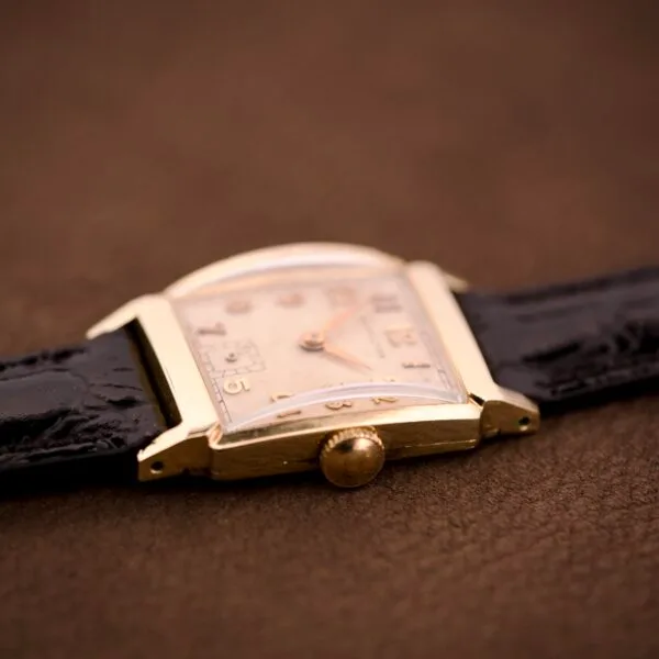 Close-up of a Hamilton Tank 14k Gold Filled Case Manual Wind Cal. 982 U.S.A. wristwatch with a black leather strap, elegantly displayed on a brown surface.