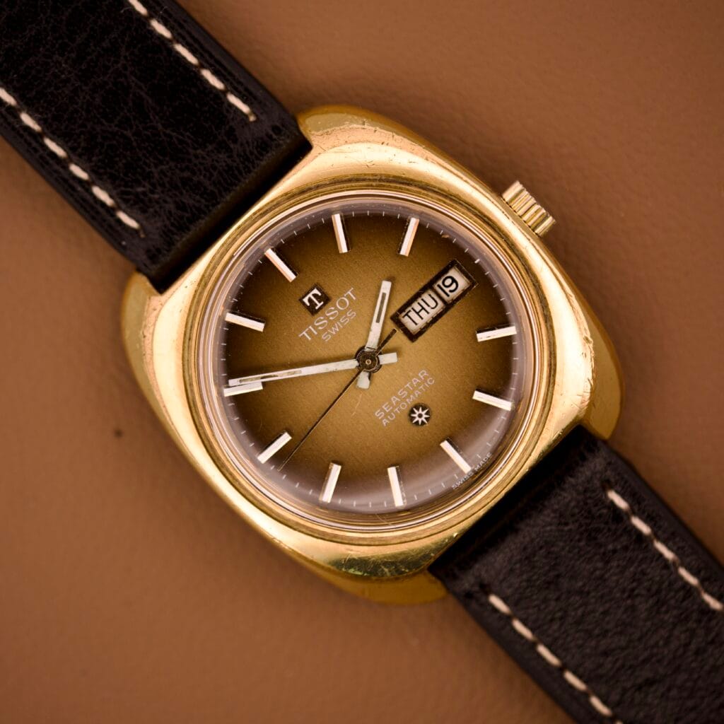 Tissot Automatic Seastar Day/Date with Brown Ombre Dial, Cal. 2571 movement, black strap on a brown background.