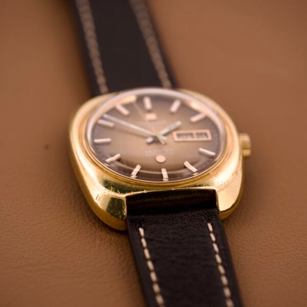 A Tissot Automatic Seastar Day/Date with a Brown Ombre Dial (Cal. 2571) and a black leather strap is displayed elegantly on a brown surface.
