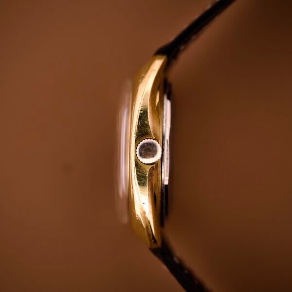 Side view of a Tissot Automatic Seastar Day / Date Cal. 2571 gold wristwatch featuring a black strap and Brown Ombre Dial, set against a brown background.