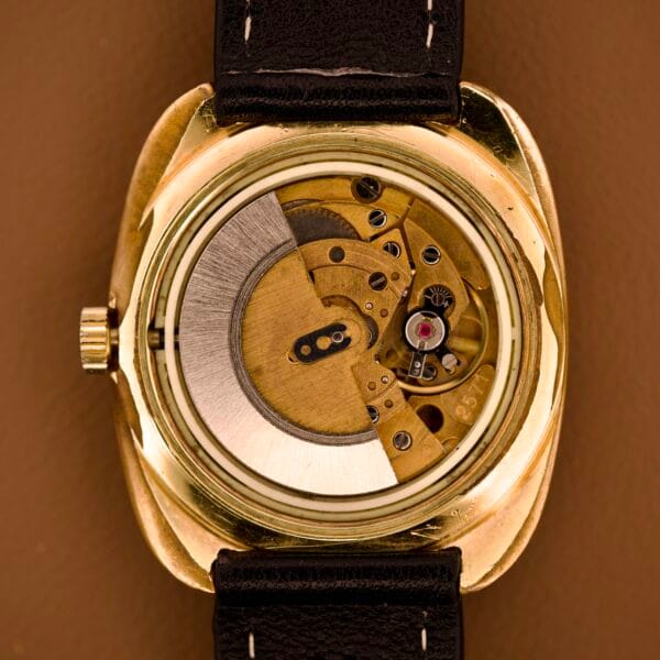 Close-up of the Tissot Automatic Seastar Day / Date Cal. 2571, showcasing its exposed mechanical movement, black leather strap, and brown ombre dial against a brown background.