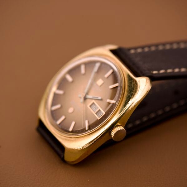 Close-up of a Tissot Automatic Seastar Day/Date with brown ombre dial (Cal. 2571) and black leather strap, displayed on a brown surface.