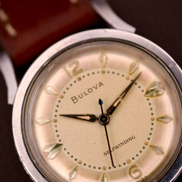 Close-up of a 1959 Bulova Self-Winding Cal. 11AFAC wristwatch featuring a stainless steel case with fancy lugs and a brown leather strap.