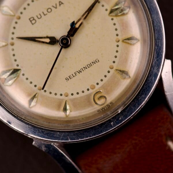 Close-up of a 1959 Bulova Self-Winding wristwatch, featuring Cal. 11AFAC movement, stainless steel case with fancy lugs, and classic dial on a leather strap.