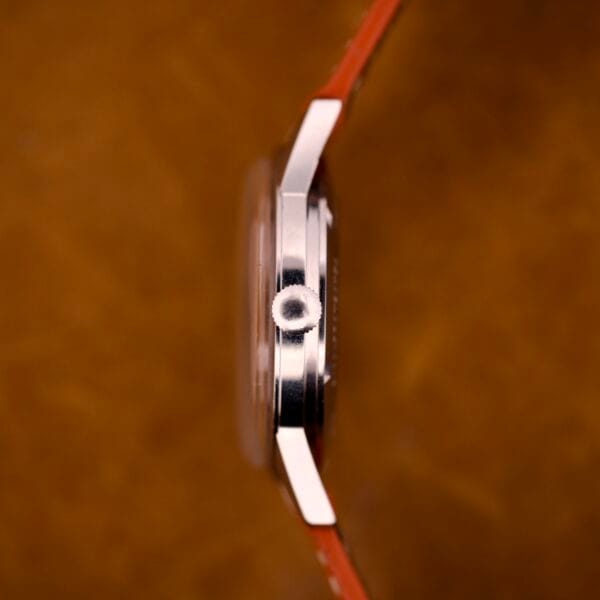 Side view of the Zodiac Hermetic Custom Manual Wind with a stainless steel case and orange strap shown against a brown background.