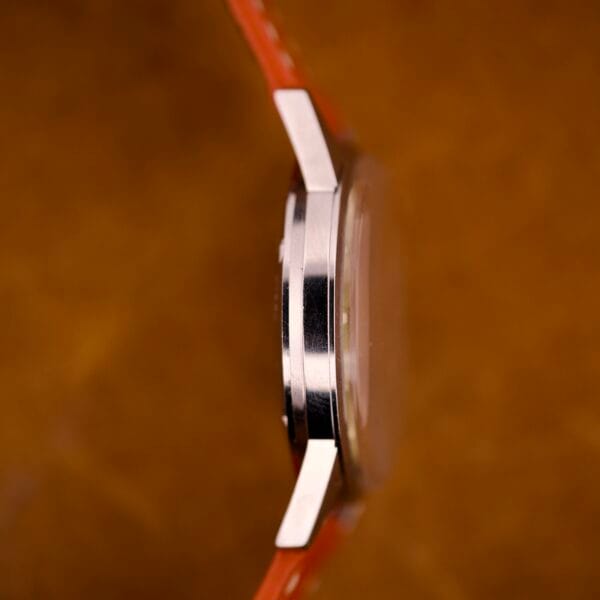 Side view of the Zodiac Hermetic Custom Manual Wind in a stainless steel case with an orange strap, set against a brown background.