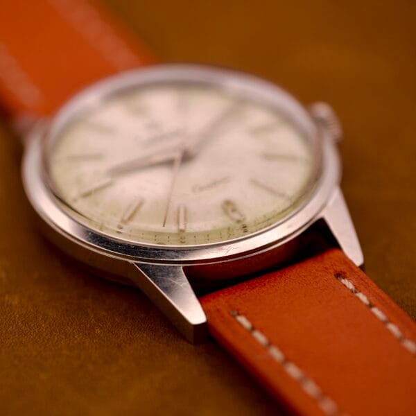 Close-up of a Zodiac Hermetic Custom Manual Wind wristwatch with a stainless steel case and an orange leather strap on a brown surface.