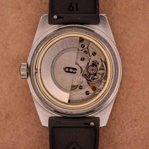 Close-up of a Tissot PR-516 "Roger Moore" Balkelite Bezel Ref. 44622, showing its exposed mechanical movement and black strap on a brown surface.