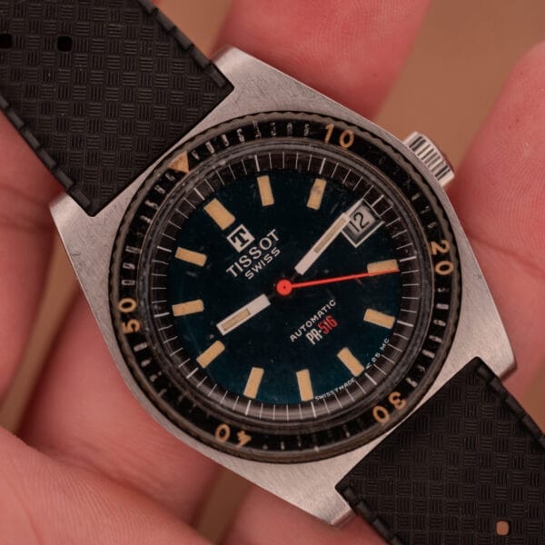 A hand holds a Tissot PR-516 "Roger Moore" Bakelite Bezel Ref. 44622, an automatic watch with a black strap and date display, known for its vintage style.