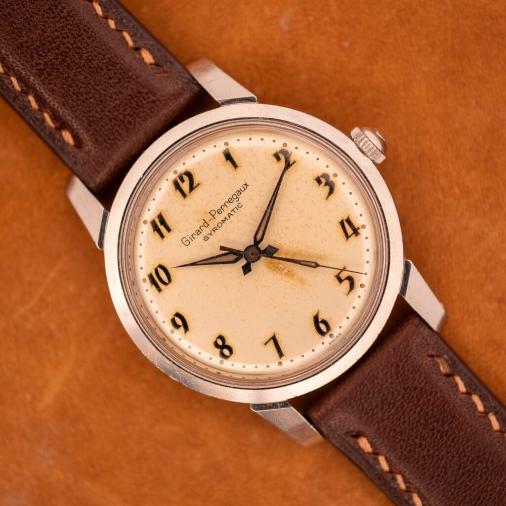 A Girard Perregaux Gyromatic in stainless steel with an Arabic numerals dial rests elegantly on a brown surface.
