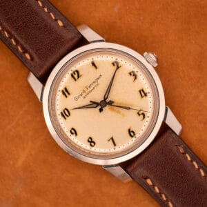 A Girard Perregaux Gyromatic in stainless steel with an Arabic numerals dial rests elegantly on a brown surface.