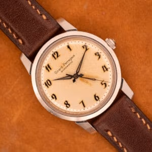 A Girard Perregaux Gyromatic in stainless steel with an Arabic numerals dial rests elegantly on a brown surface.