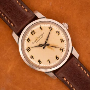 A Girard Perregaux Gyromatic in stainless steel with an Arabic numerals dial rests elegantly on a brown surface.