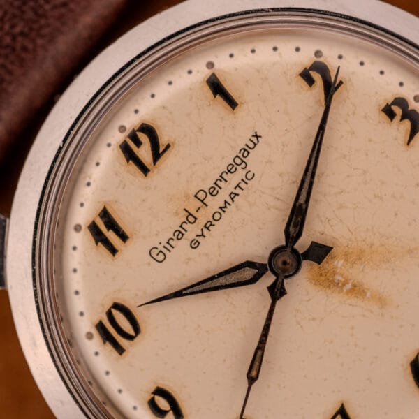 Close-up of a vintage Girard Perregaux Gyromatic in stainless steel, featuring an aged Arabic numerals dial with dark hands.