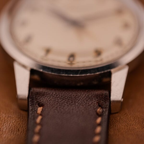 Close-up of a vintage Girard Perregaux Gyromatic with stainless steel case, Arabic numerals dial, and brown leather strap featuring stitched detailing.