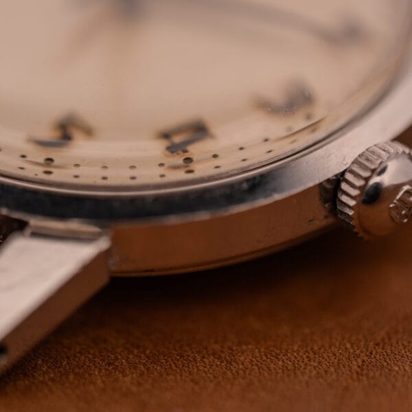 Close-up of a Girard Perregaux Gyromatic in stainless steel, featuring an Arabic numerals dial, crown, and case resting on a brown surface.