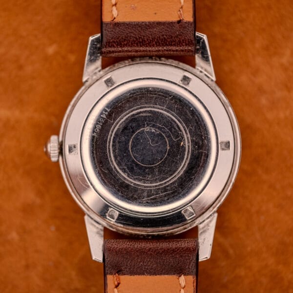 Back view of a vintage Girard Perregaux Gyromatic in Stainless Steel with Arabic numerals dial and brown leather strap, displayed on a brown surface.