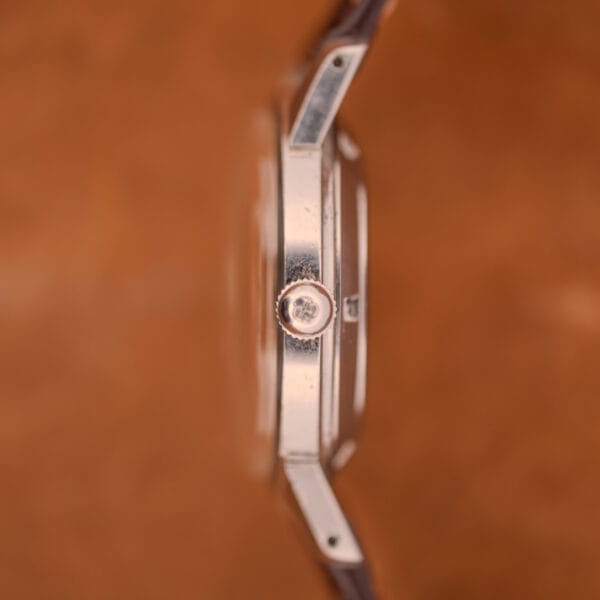 Close-up side view of a Girard Perregaux Gyromatic in Stainless Steel with Arabic numerals dial and visible crown, set against a blurred brown background.