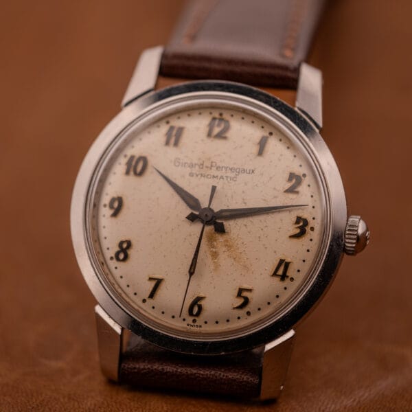 A vintage Girard Perregaux Gyromatic with a stainless steel case, leather strap, and Arabic numerals dial.