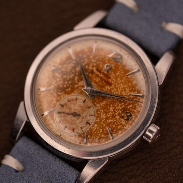 Close-up of an Omega Seamaster Automatic Tropic Dial Ref. 2848 Cal. 490 wristwatch with a speckled, rusted finish and blue leather strap, displayed on a brown surface.