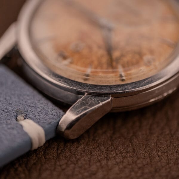 Close-up of an Omega Seamaster Automatic Tropic Dial Ref. 2848 with Cal. 490 movement, showcasing a worn dial and blue leather strap on a brown textured surface.