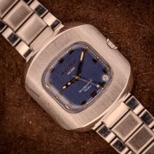 A Movado HS 360 Kingmatic Video Blue Dial Ref. 409-705 Cal. 408 wristwatch with a blue square dial and silver metal band, displayed on a brown surface.