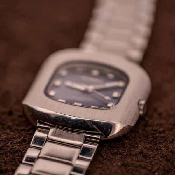 A silver square watch featuring a blue dial, inspired by the iconic Movado HS 360 Kingmatic Video Ref. 409-705 Cal. 408 design.