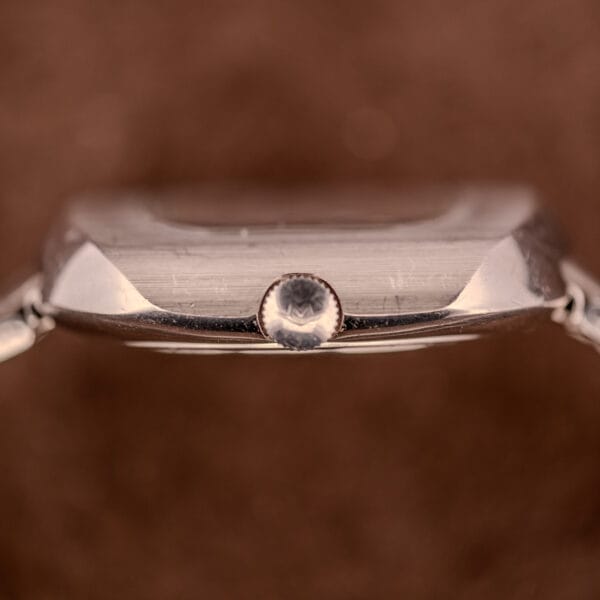 Close-up side view of the crown on a Movado HS 360 Kingmatic Video Blue Dial Ref. 409-705 Cal. 408 silver wristwatch against a blurred brown background.