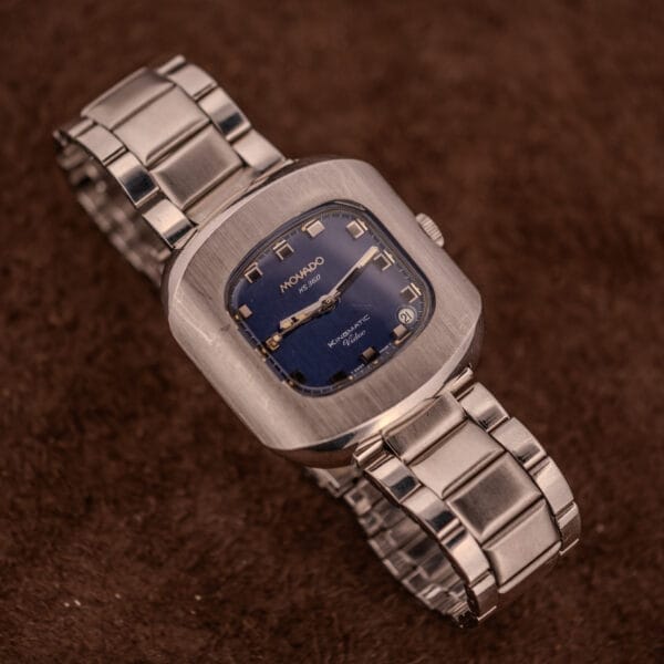 A Movado HS 360 Kingmatic Video Blue Dial Ref. 409-705 Cal. 408 wristwatch with a vivid blue square dial is displayed on a brown textured surface.