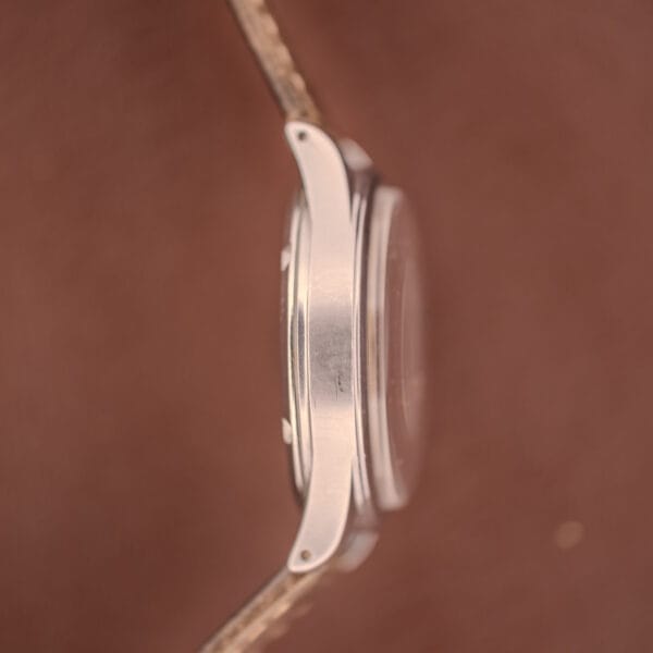 Side view of an Omega WWII Era Military "US ARMY" Ref. 2179 stainless steel wristwatch with brown leather strap and Cal. 30T2 SC movement, set against a blurred brown background.