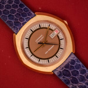 A vintage Longines Olympian High Frequency Ref. 3141 watch with Cal. 6972 movement, gold case, purple strap, and day-date display on a red background.