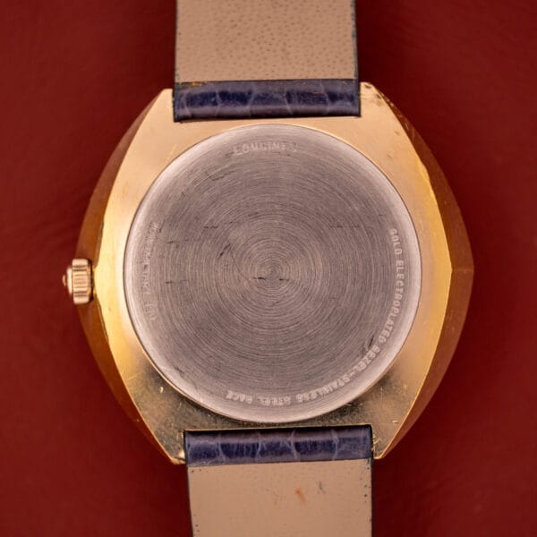 Close-up of the back of a Longines Olympian High Frequency Ref. 3141 Cal. 6972 gold wristwatch with a leather strap, resting on a reddish surface.